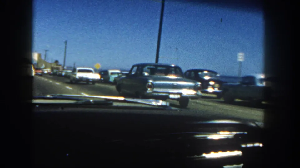 In-car 1962 San Diego frame with early 1960s cars beside a coastal highway and water visible in the distance.