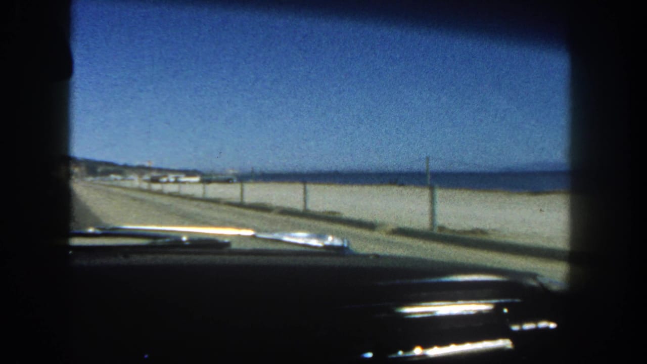 View through a car windshield along a coastal road beside a beach and ocean.