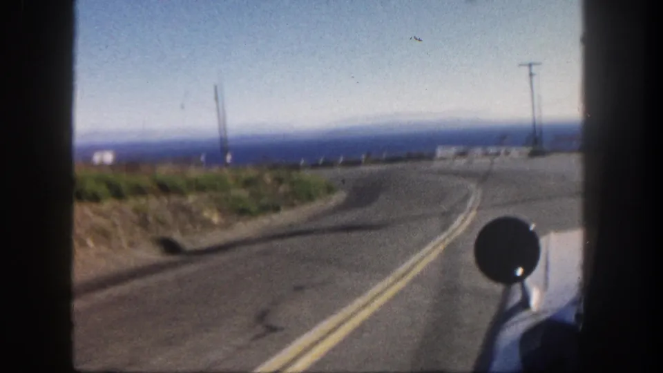 1962 San Diego coastal driving view with an open two-lane road, Pacific horizon, roadside slope, and utility poles.