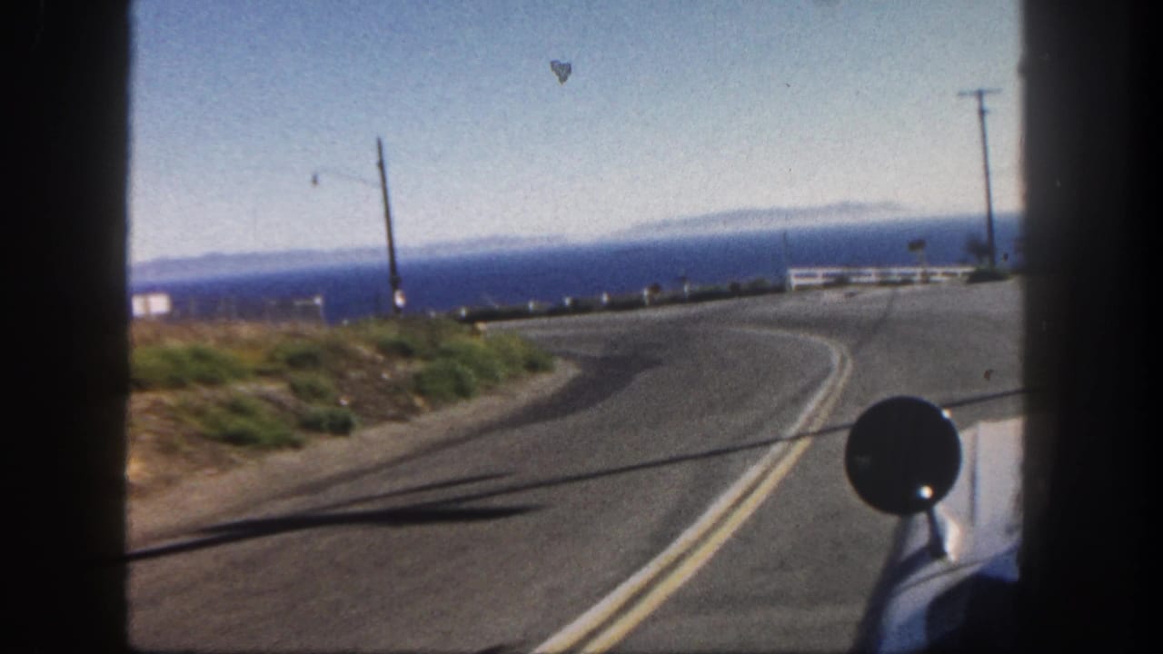 Curving coastal road seen from inside a car, with ocean horizon, guardrail, utility poles, and side mirror.