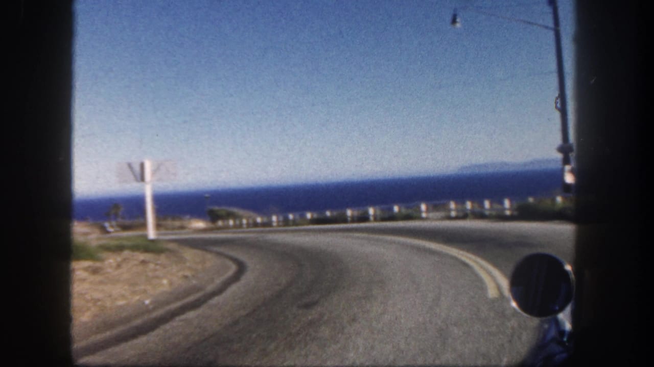 San Diego coastal road footage from 1962 shows a right-hand curve above the ocean with guardrail posts, roadside sign, and vehicle mirror.