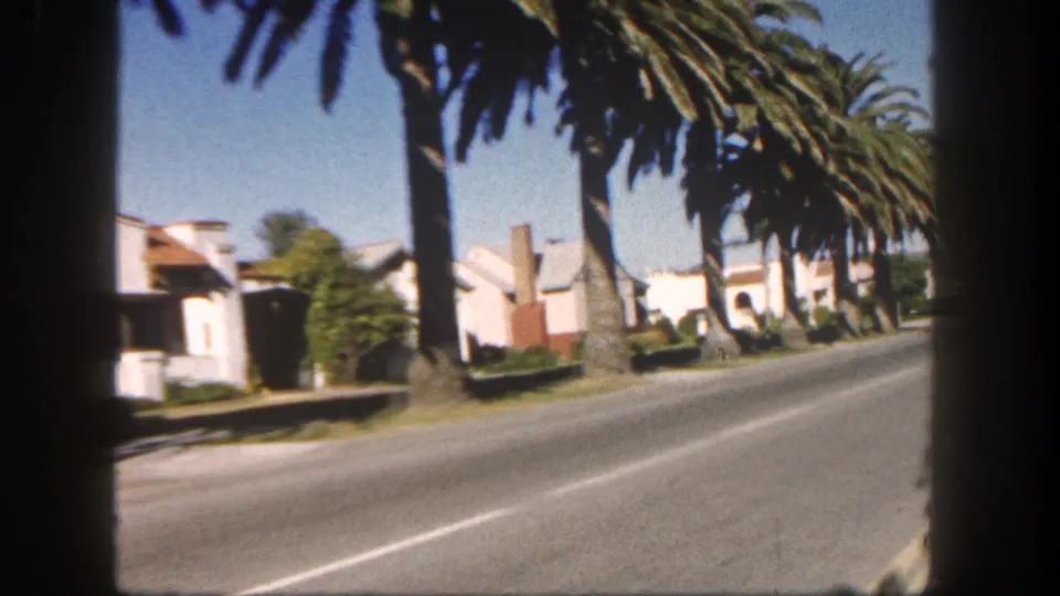 1962 San Diego street view with tall palms, angled roadway, sidewalks, and low residential houses filmed from a moving car.