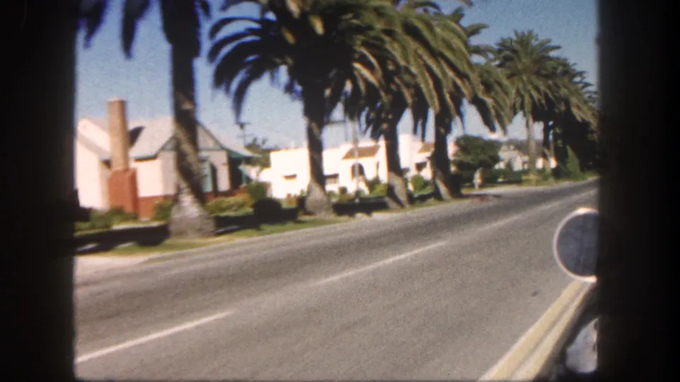 Final frame of a 1962 San Diego drive past palm trees, stucco houses, lawns, and a broad residential road.