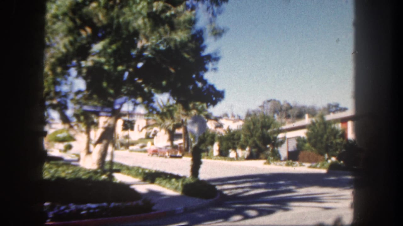 1962 San Diego residential street with palms, single-story houses, driveway areas, and a light-colored car near the curb.