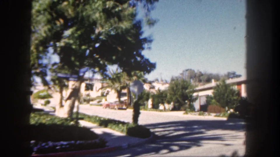 1962 San Diego residential street with palms, single-story houses, driveway areas, and a light-colored car near the curb.