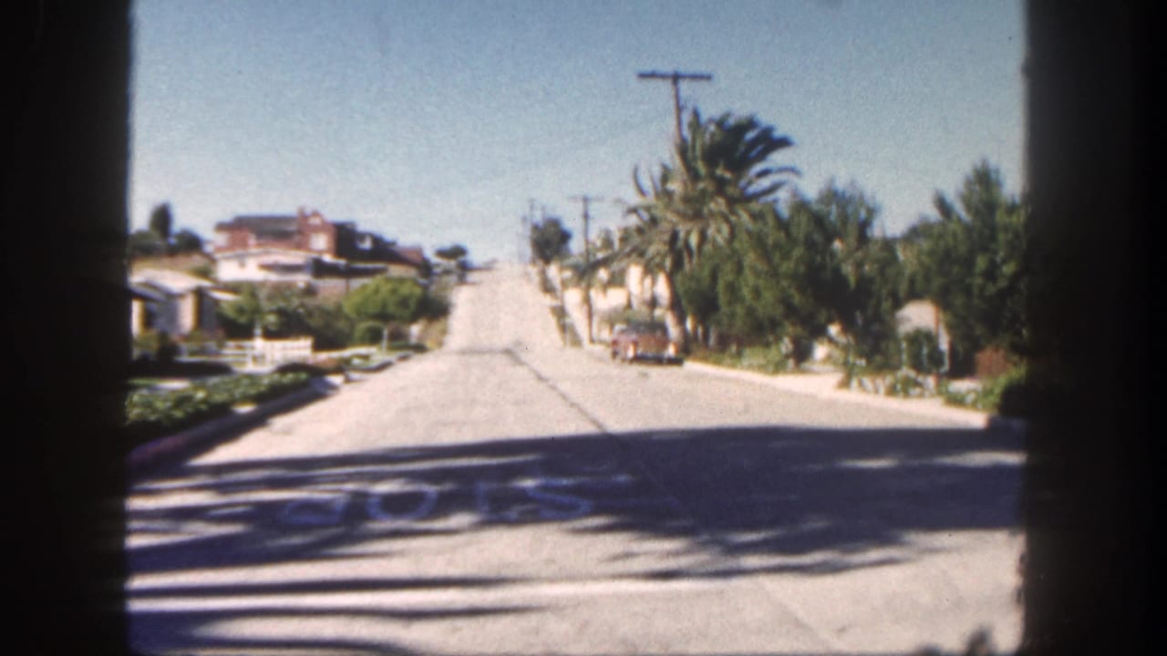 1962 San Diego residential street with palm trees, low houses, utility poles, and bright sun, filmed from behind window bars.