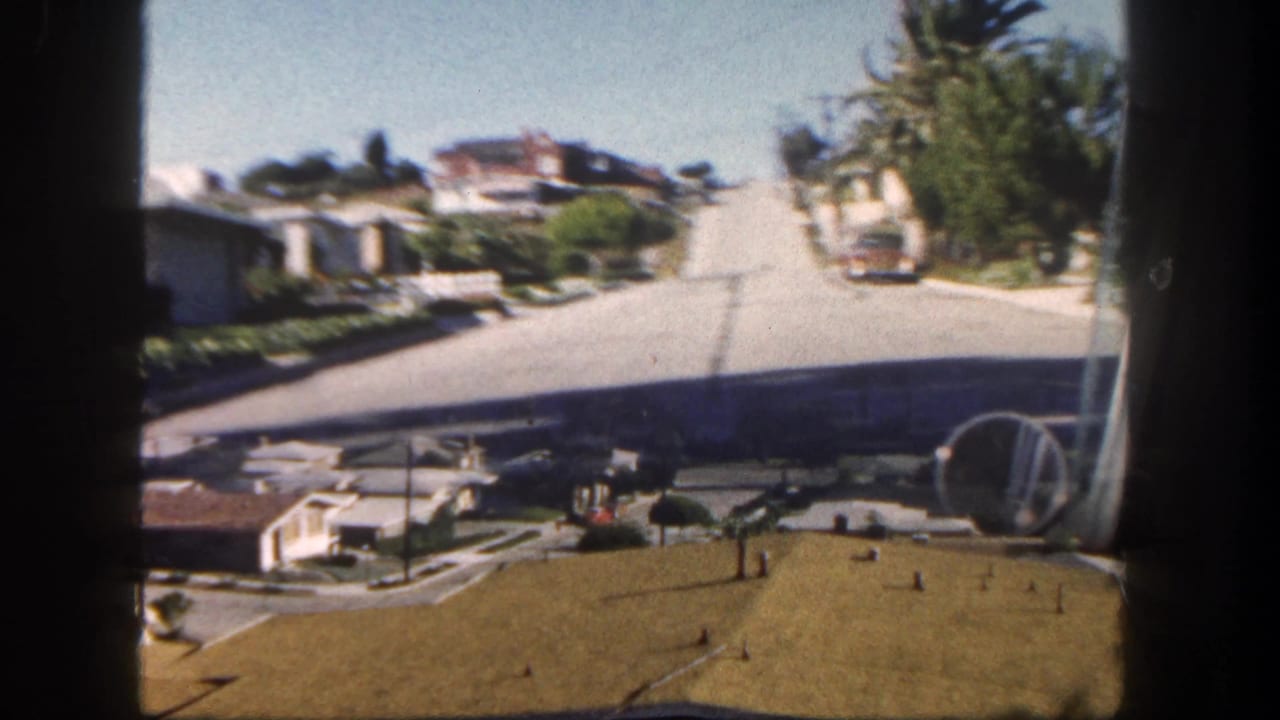 San Diego coastal neighborhood view with rooftops, street, palms, ocean horizon, and distant landforms, seen through window bars.