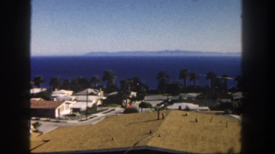 1962 San Diego ocean outlook with neighborhood rooftops, palms, clear sky, and distant landforms across the water.