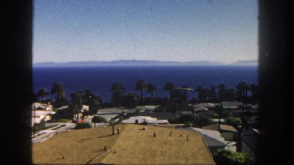 Soft 8mm frame from 1962 San Diego showing rooftops and palms below a wide blue ocean horizon.