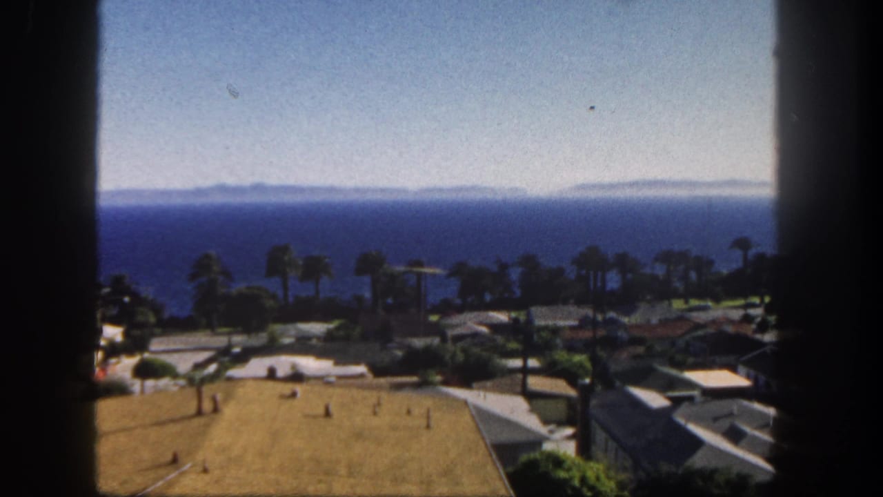 1962 San Diego coastal town view with single-story homes, palms, lawns, and a blue ocean horizon seen through a dark foreground divider.