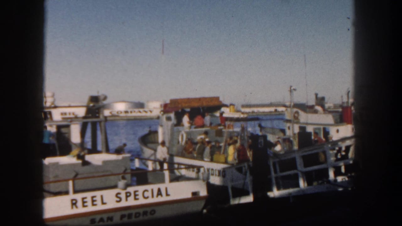 Fishing boat at a San Diego dock with people boarding and Mobil tanks across the water.