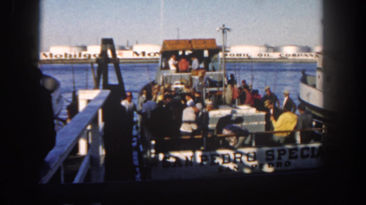 Crowded ferry deck at a bay dock with Mobil Oil tanks in the background.