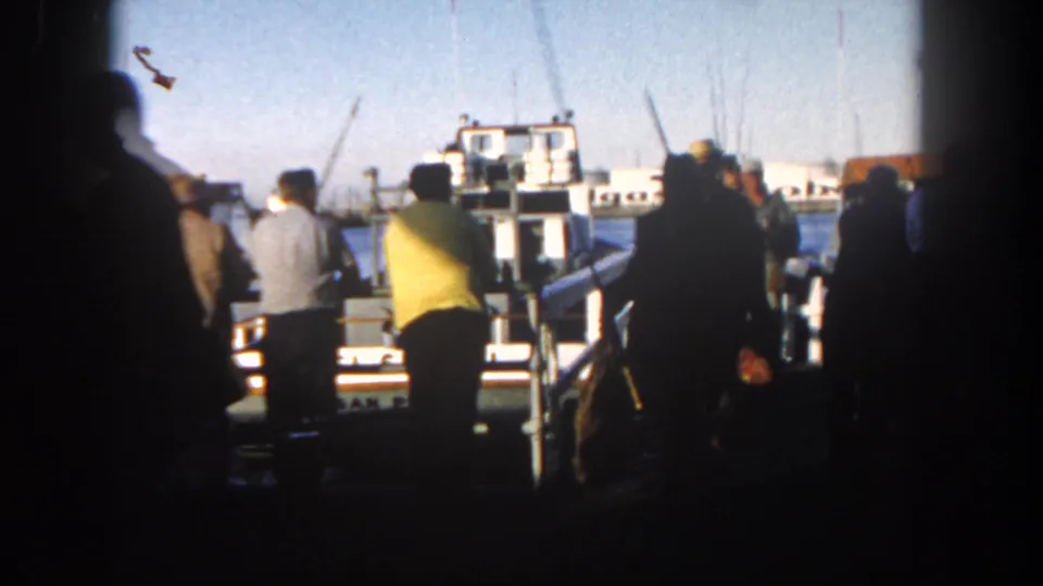 At the end of the clip, passengers remain gathered near the San Diego harbor boat, framed by dark film edges and distant industrial waterfront details.