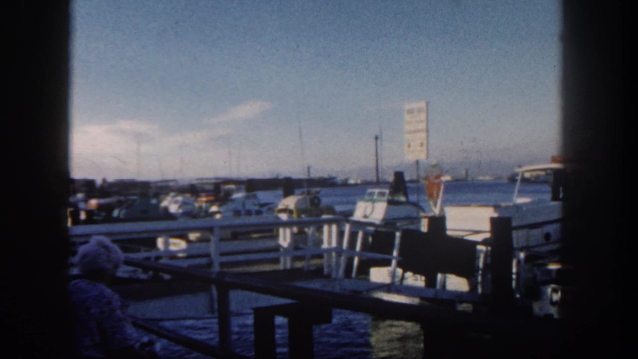 Small boats docked at a pier with a seated person in the shaded foreground.