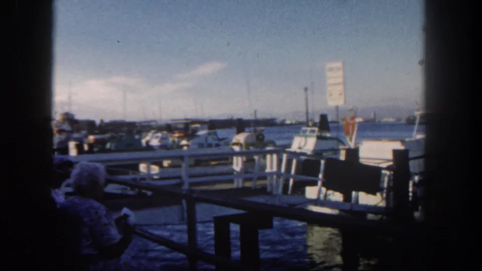 The final frame holds on the 1962 San Diego marina, with boats along the pier and a seated foreground figure partly silhouetted by shade.