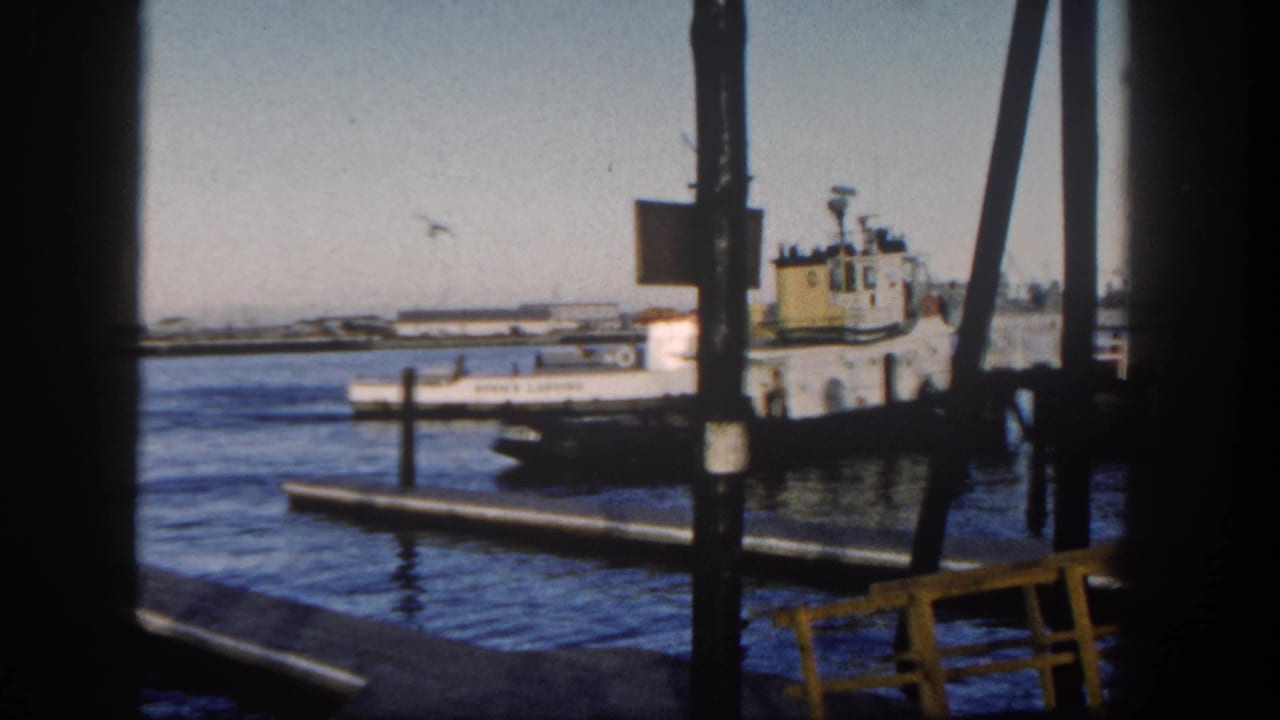 Tugboat docked at a harbor pier, seen through dark vertical beams over blue water.