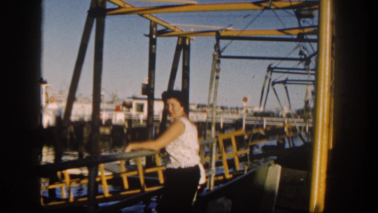 Woman in a sleeveless top leaning on a yellow boat railing near harbor water.
