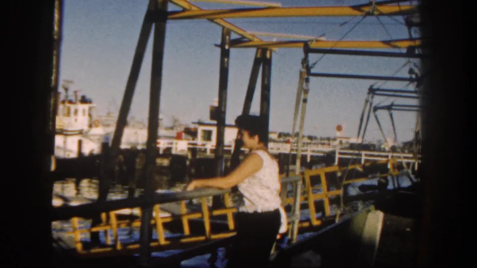 The woman appears in profile at a yellow waterfront railing, with San Diego harbor water, moored boats, and pier structures in view.