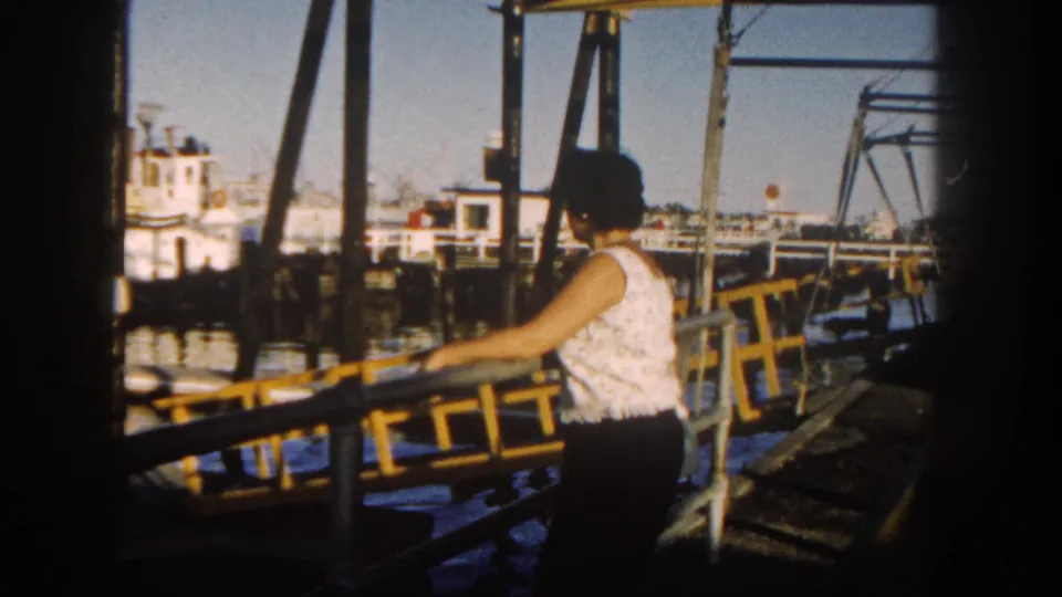 Woman on a San Diego waterfront pier in 1962, turned toward the harbor amid railings and boats.