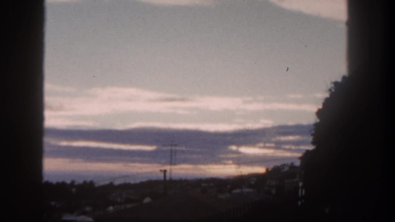 Dim sunrise behind layered clouds with silhouetted rooftops and utility poles.
