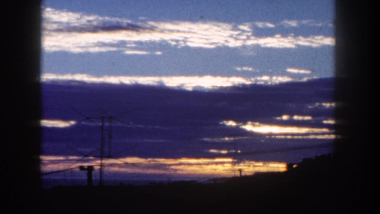 1962 San Diego home-movie frame with streaked clouds, warm low light, and silhouetted utility lines near the horizon.