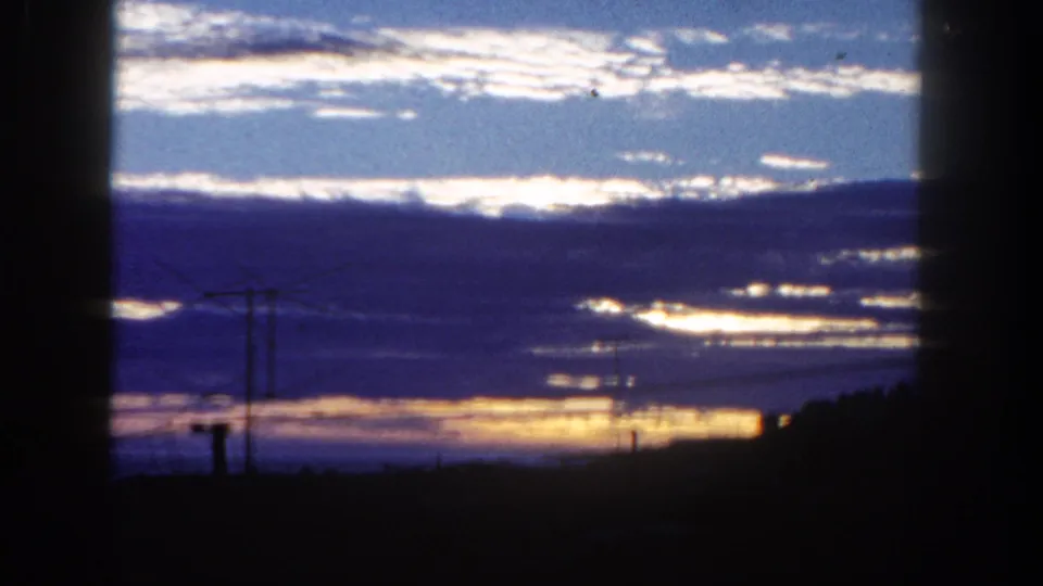 1962 San Diego 8mm view of layered clouds and low orange light, with poles and wires silhouetted against the sky.