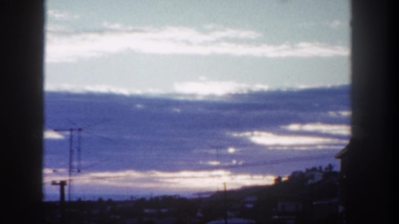 Clouded twilight sky over a dark town horizon with utility poles and vertical foreground framing.