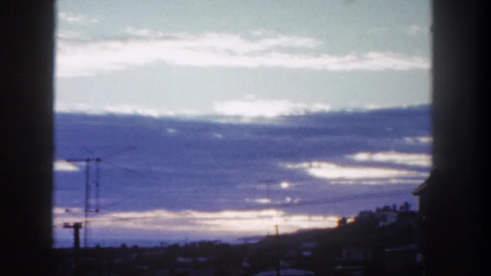 1962 8mm San Diego home-movie frame showing a glowing sky, silhouetted poles, power lines, rooftops, and dark window-like edges.