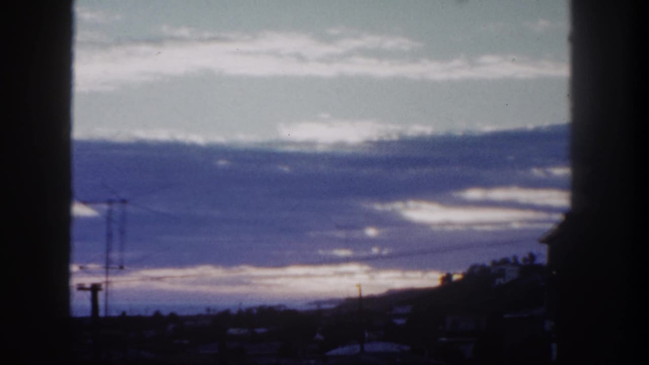 Dim horizon with layered clouds, power lines, and silhouetted buildings framed by dark vertical edges.