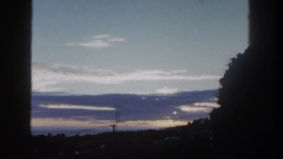 1962 San Diego 8mm frame showing a dim sunset horizon, layered clouds, distant hills, utility poles, and dark foreground framing.