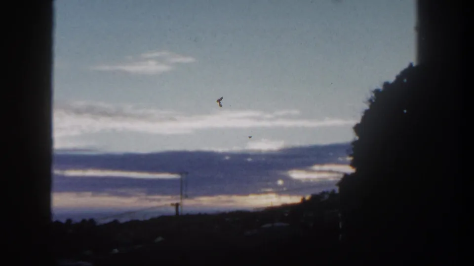 1962 San Diego 8mm still showing a softly exposed sunset over hills, with utility poles below and dark window-like framing.