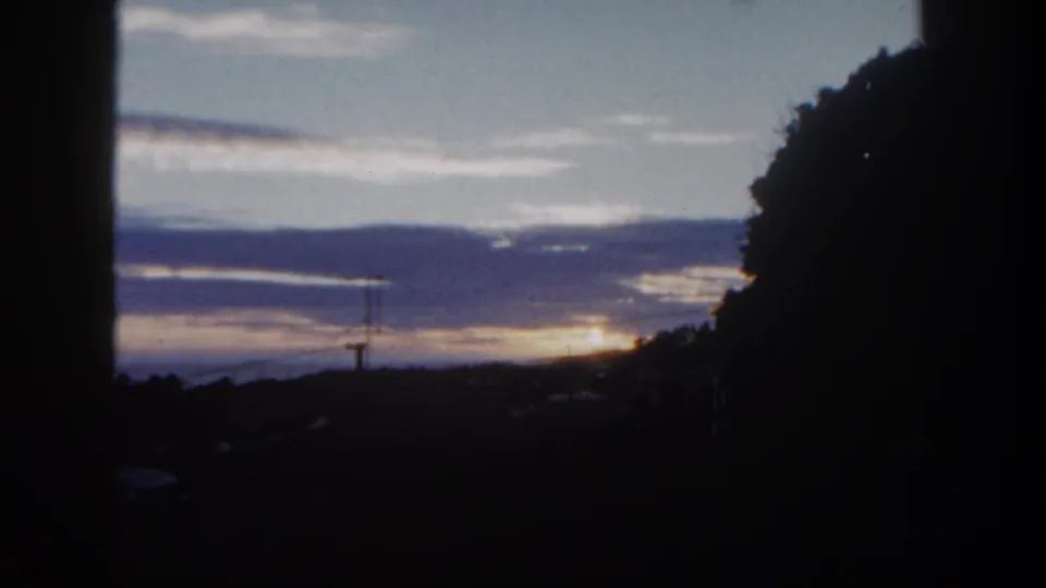 1962 San Diego frame with dusk clouds, a warm horizon, hillside silhouettes, and heavy dark foreground framing from a nearby structure or tree.