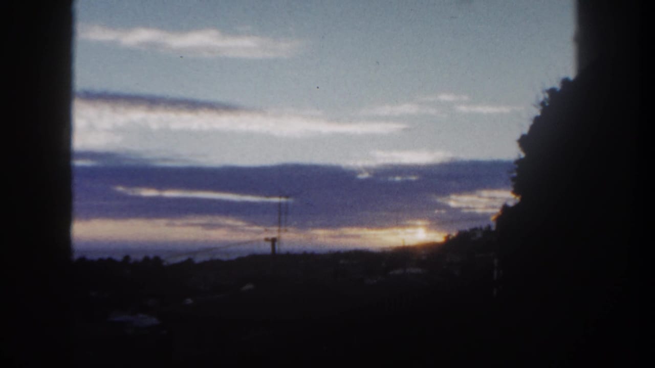 1962 San Diego frame with the sun low under cloud bands, silhouetted trees, and utility lines on the horizon.