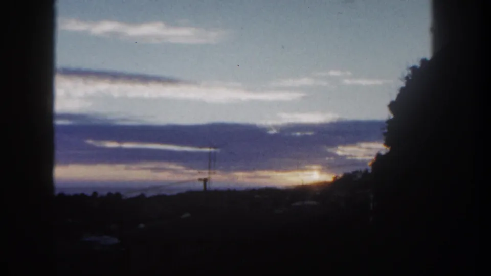 1962 San Diego frame with the sun low under cloud bands, silhouetted trees, and utility lines on the horizon.