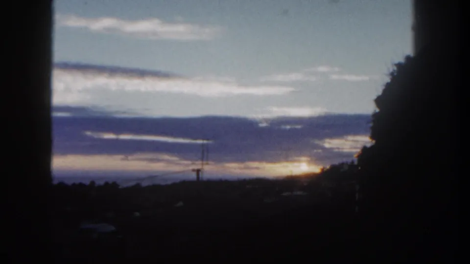 Soft 1962 8mm San Diego view of a bright horizon, layered clouds, dark trees, and a foreground edge.