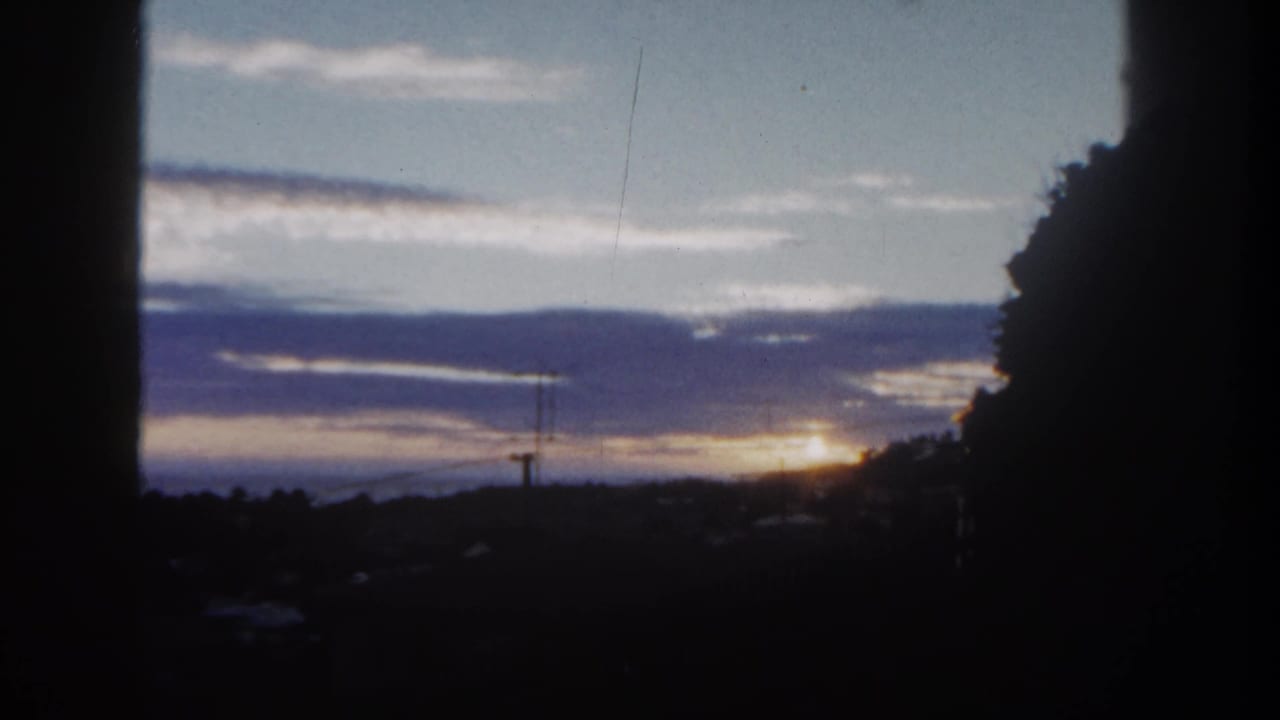 Sunset over a dark city horizon with silhouetted trees, clouds, and 8mm frame borders.