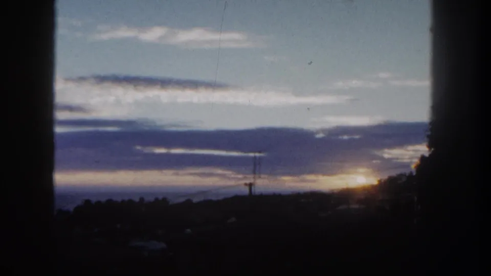 1962 San Diego home-movie frame holding on a cloudy sunset over a dark urban horizon with trees and a utility pole.