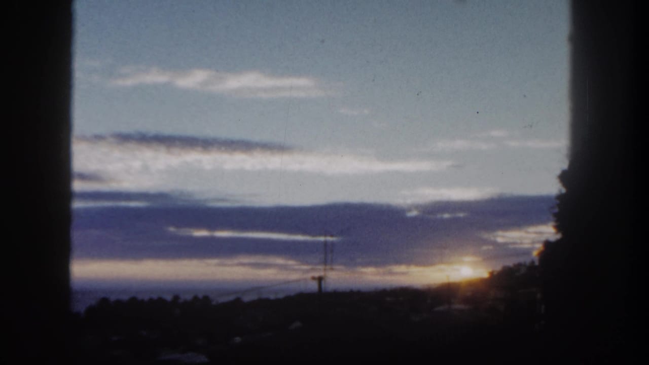 1962 8mm view of a San Diego sunrise, with the sun near the horizon behind silhouetted coastal hills and cloud bands.