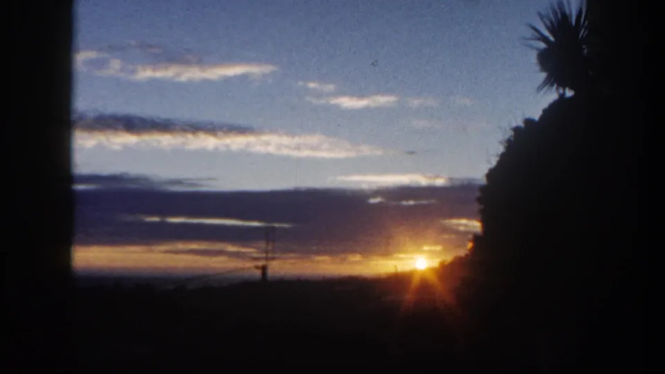 Late frame of the 1962 San Diego sunrise, with golden flare at the horizon, dark hillside, palm silhouette, and cloud layers.