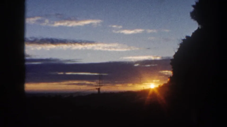 1962 San Diego 8mm frame showing a soft, low sunset with dark foreground trees, clouds, and a shadowed horizon.