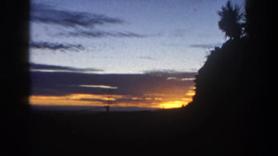 1962 San Diego-area 8mm frame showing the sunset dimming behind silhouetted trees, with a small antenna visible against the sky.