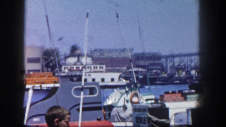 1962 San Diego marina view with boats, masts, dock structures, and a person partly visible near the foreground.