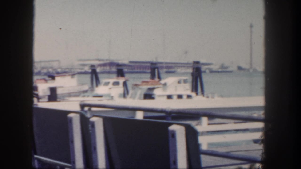 Pier railing and benches frame docked boats with water and shoreline beyond.