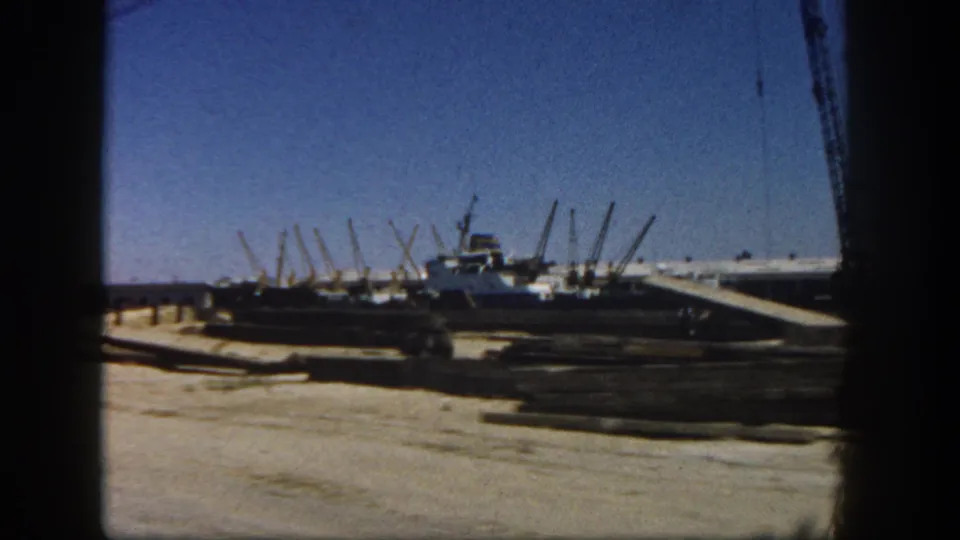 1962 San Diego 8mm frame showing a dirt construction area, crane equipment, and harbor-adjacent industrial structures.