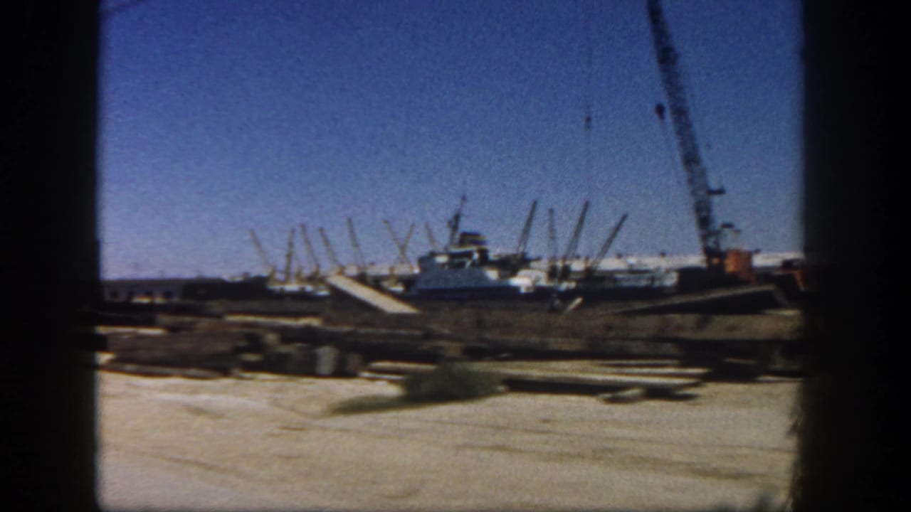 1962 San Diego frame with crane equipment, low industrial structures, and materials spread across a dirt construction site.