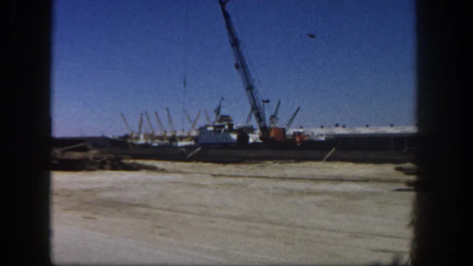 1962 San Diego 8mm frame with a wide harbor-side construction view, crane boom, dirt lot, and low industrial forms.