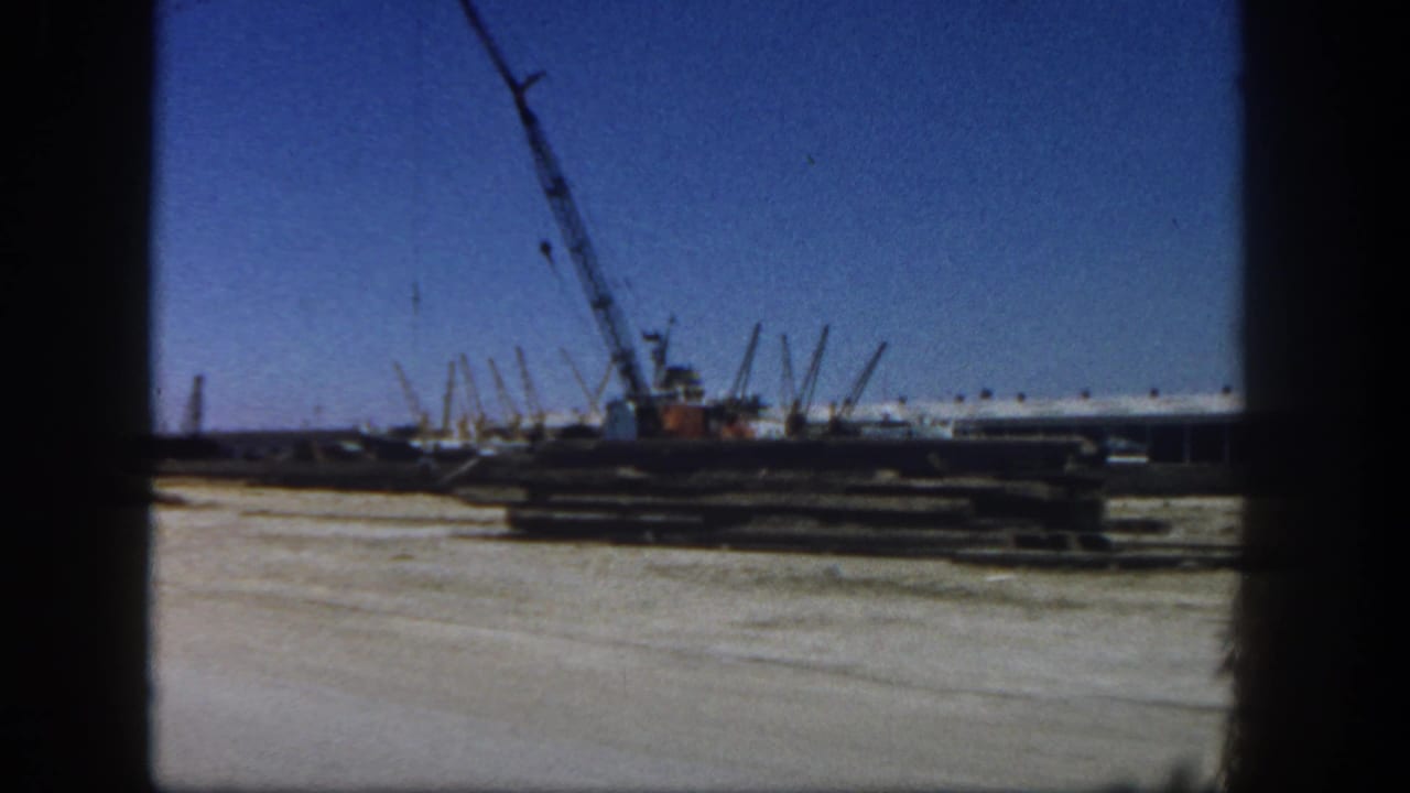 A San Diego waterfront construction area with a crane, stacked materials, and marina structures visible in a 1962 8mm frame.
