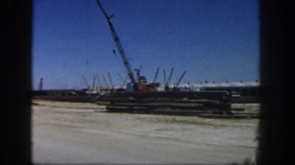 A San Diego waterfront construction area with a crane, stacked materials, and marina structures visible in a 1962 8mm frame.