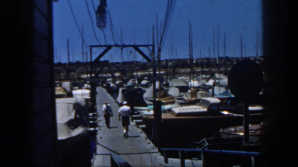 1962 San Diego marina view with moored sailboats, many masts, and two adult men walking along a wooden dock.