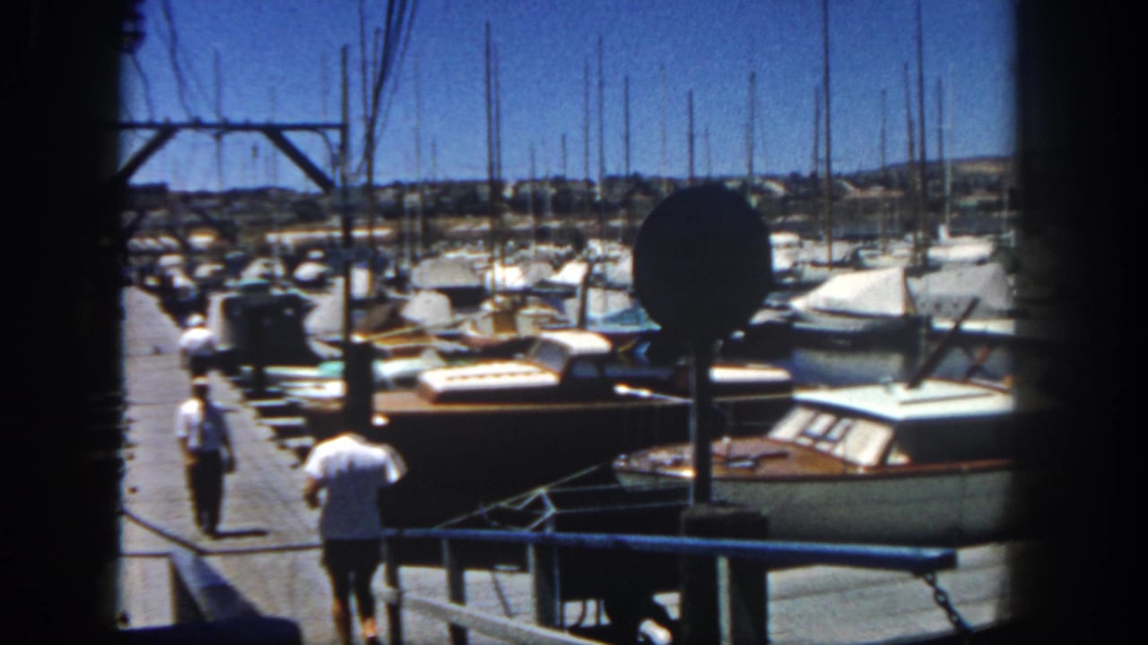 The man continues running along the San Diego marina dock, passing rows of boats under a bright blue sky.